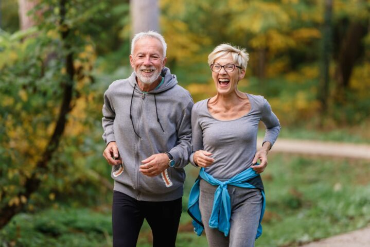 Cheerful active senior couple jogging in the park. Exercise toge